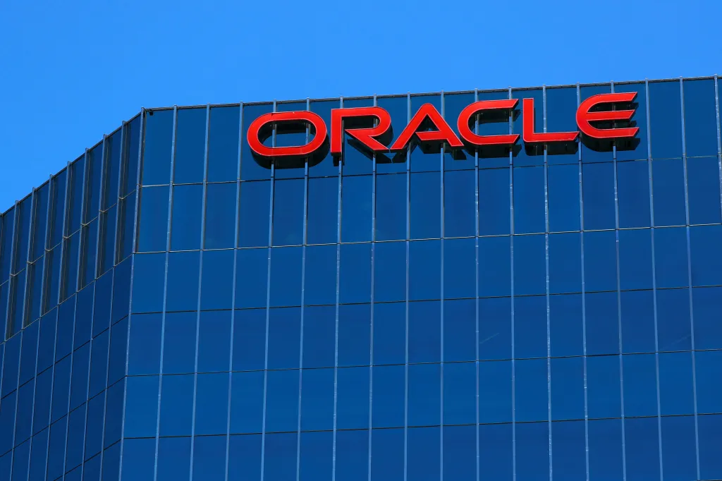 The Oracle logo is displayed in red letters on a blue glass office building.