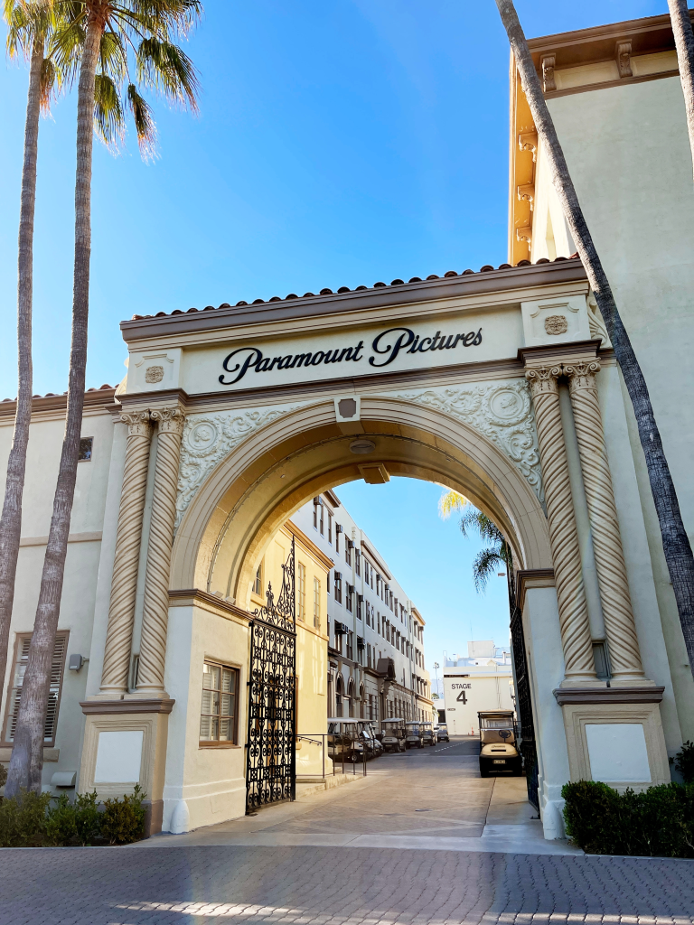 Paramount Pictures Bronson Gate with the company logo at the top, a blue sky, and palm trees in Hollywood, California.