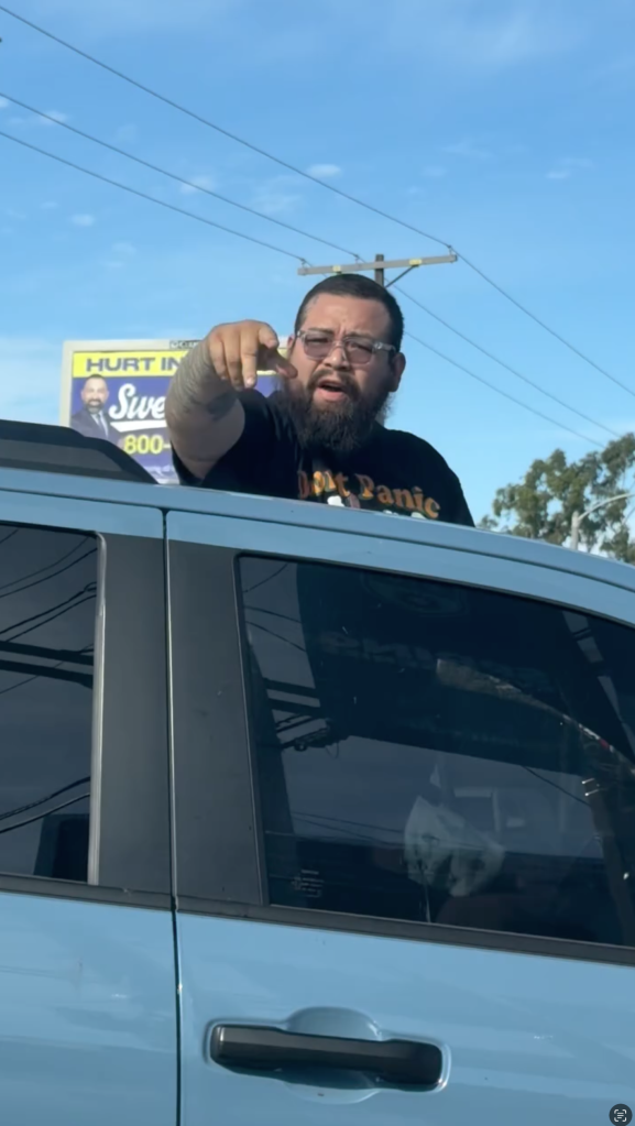 A man leaning out of a car window, pointing.