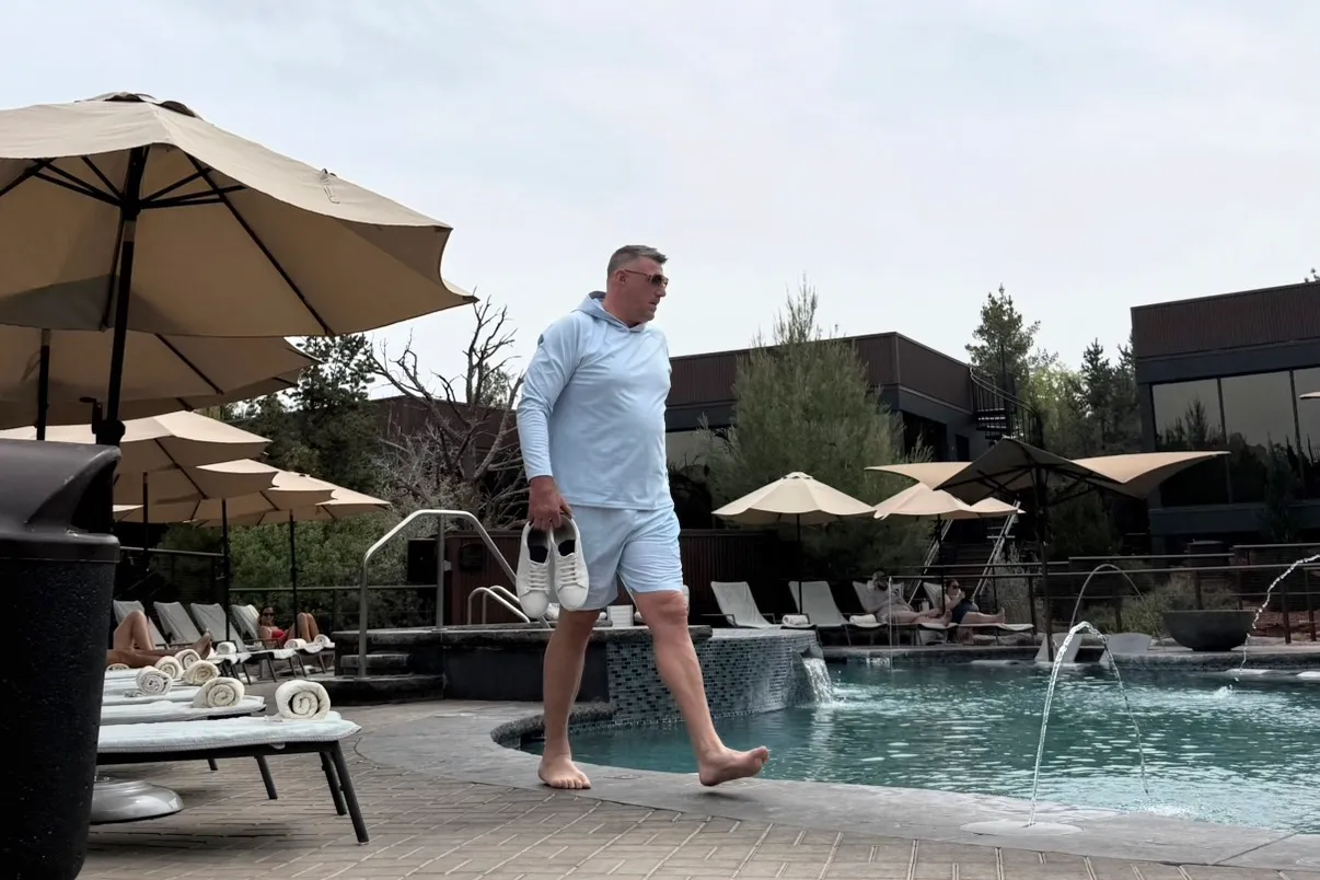 Mike Vrabel walks barefoot by the pool at Ambiente Sedona hotel, holding his shoes.