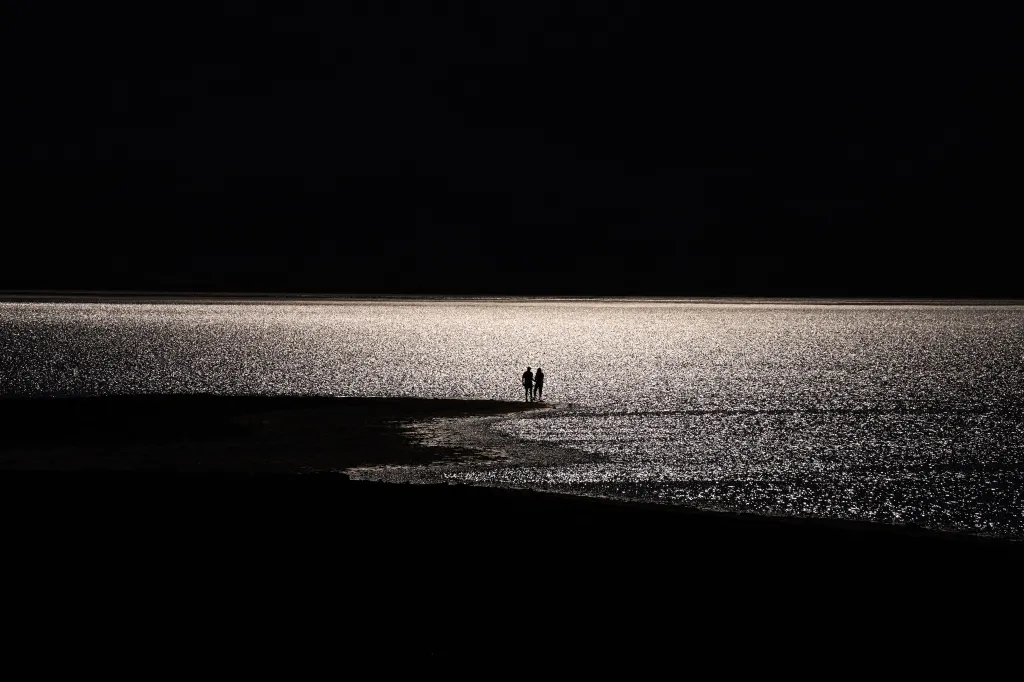 Two silhouettes standing on the edge of a shimmering lake.
