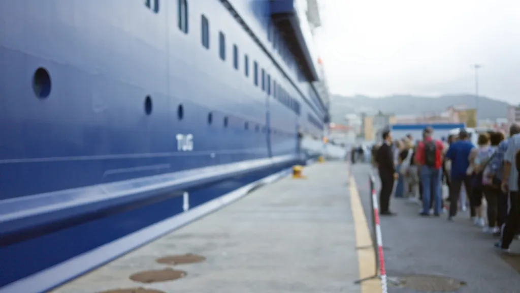 Blurred image of people queuing at a cruise port, with a large blue ship in the background.
