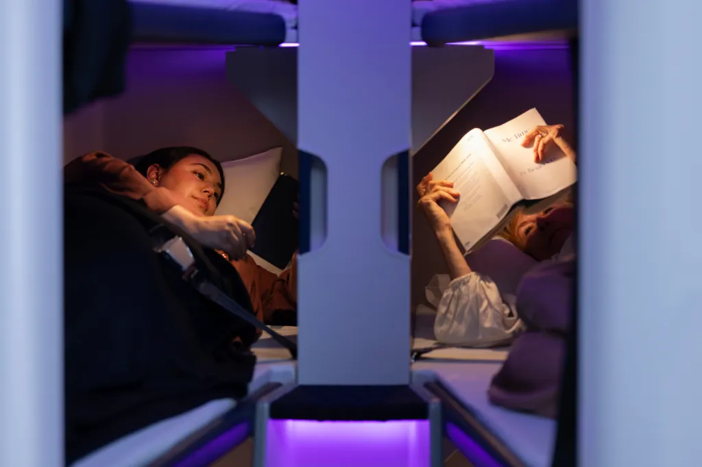 Two women in sleeping pods with purple ambient lighting.