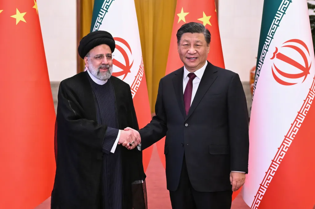 Iranian President Ebrahim Raisi and Chinese President Xi Jinping shake hands in front of their national flags.