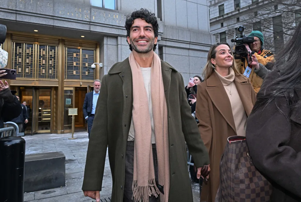 Justin Baldoni smiles while leaving federal court after a settlement conference.