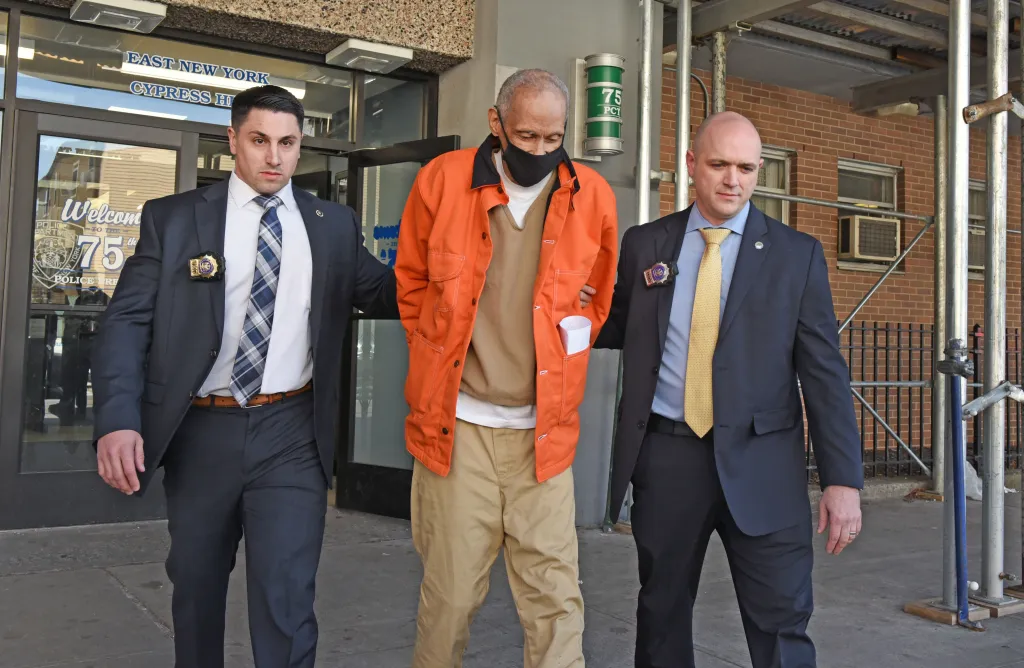 Harvey Marcelin, in an orange jacket and black mask, is escorted by two detectives after being charged with murder.