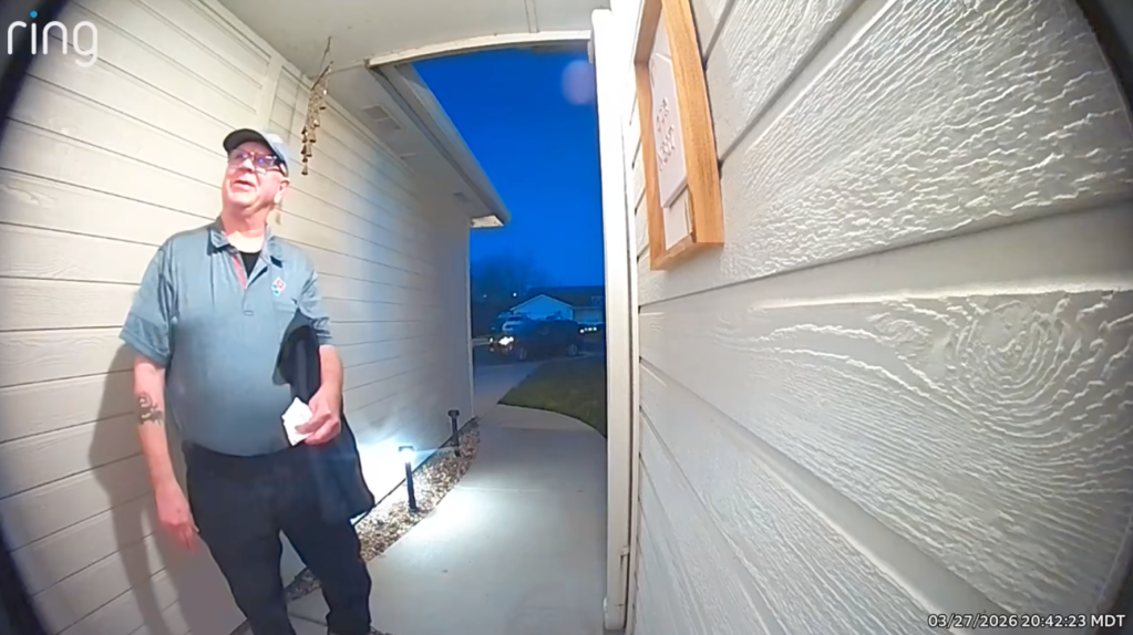 A Domino's pizza delivery driver standing on a porch.