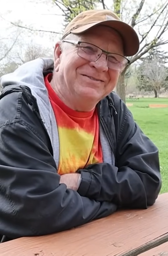 An older man in glasses and a cap, smiling at the camera.