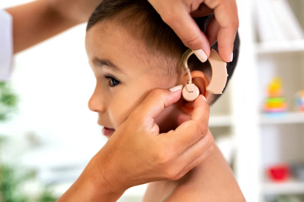 Doctor placing a hearing aid on a child's ear.