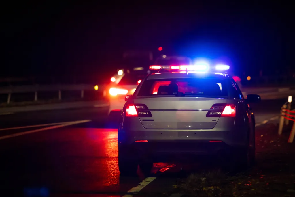 Police car with flashing red and blue emergency lights at night on a highway.