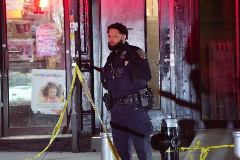 A police officer in uniform stands behind yellow caution tape at the scene of a police-involved shooting.