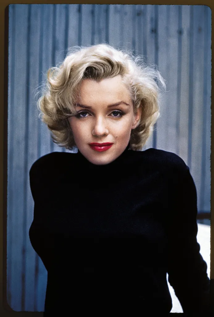 Portrait of actress Marilyn Monroe with blonde curls and red lipstick, wearing a black top.