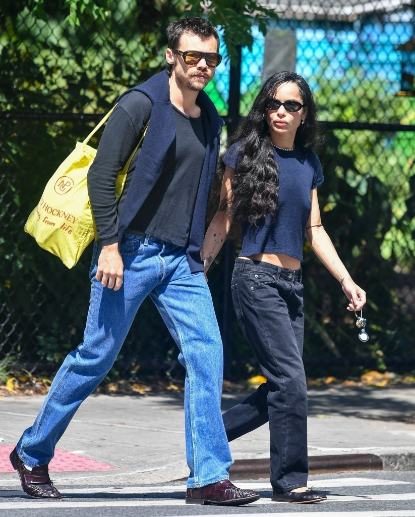 Harry Styles and Zoë Kravitz holding hands while walking outside in blue and black jeans.