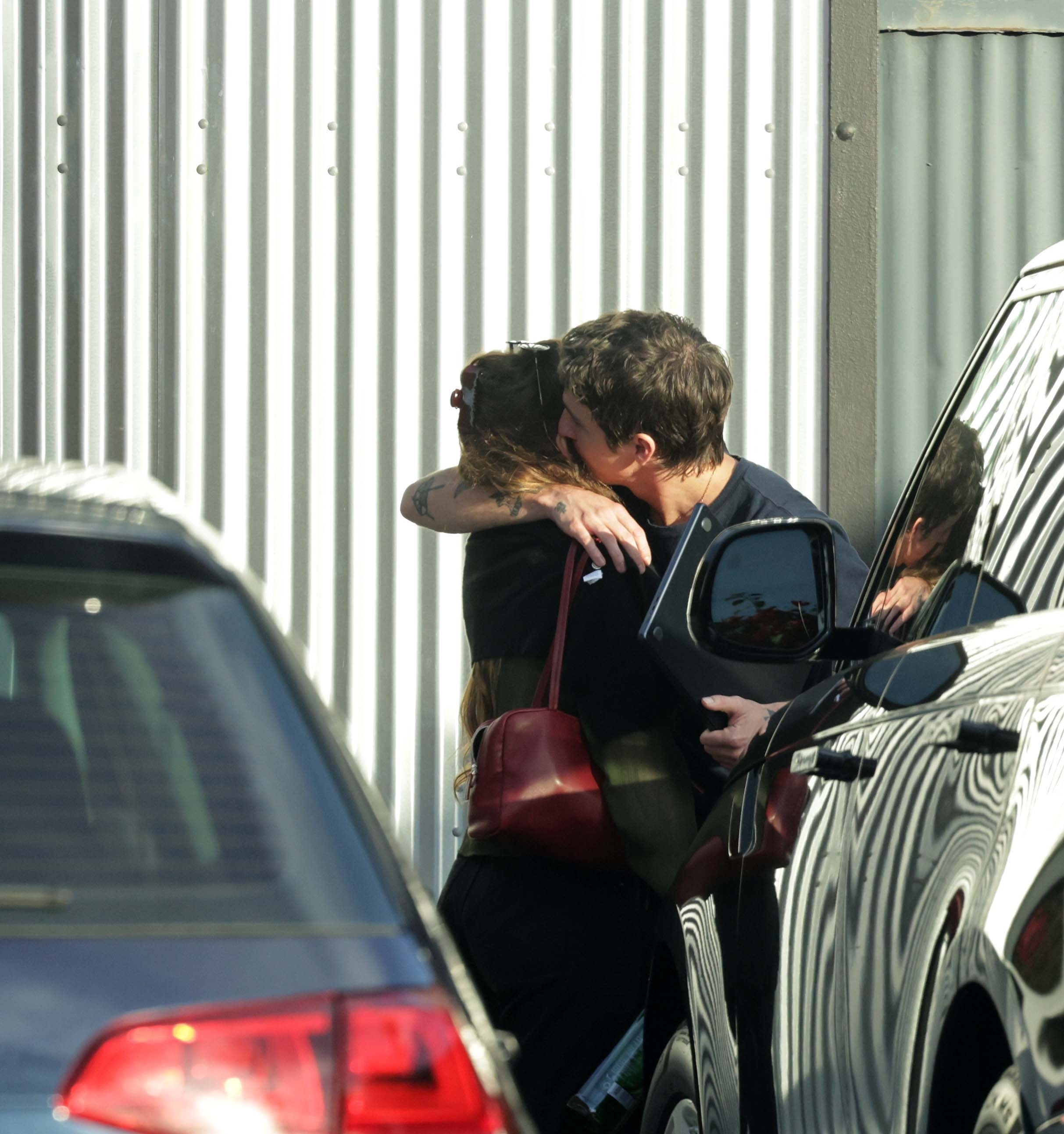 Dakota Johnson and Role Model in an embrace, next to cars.