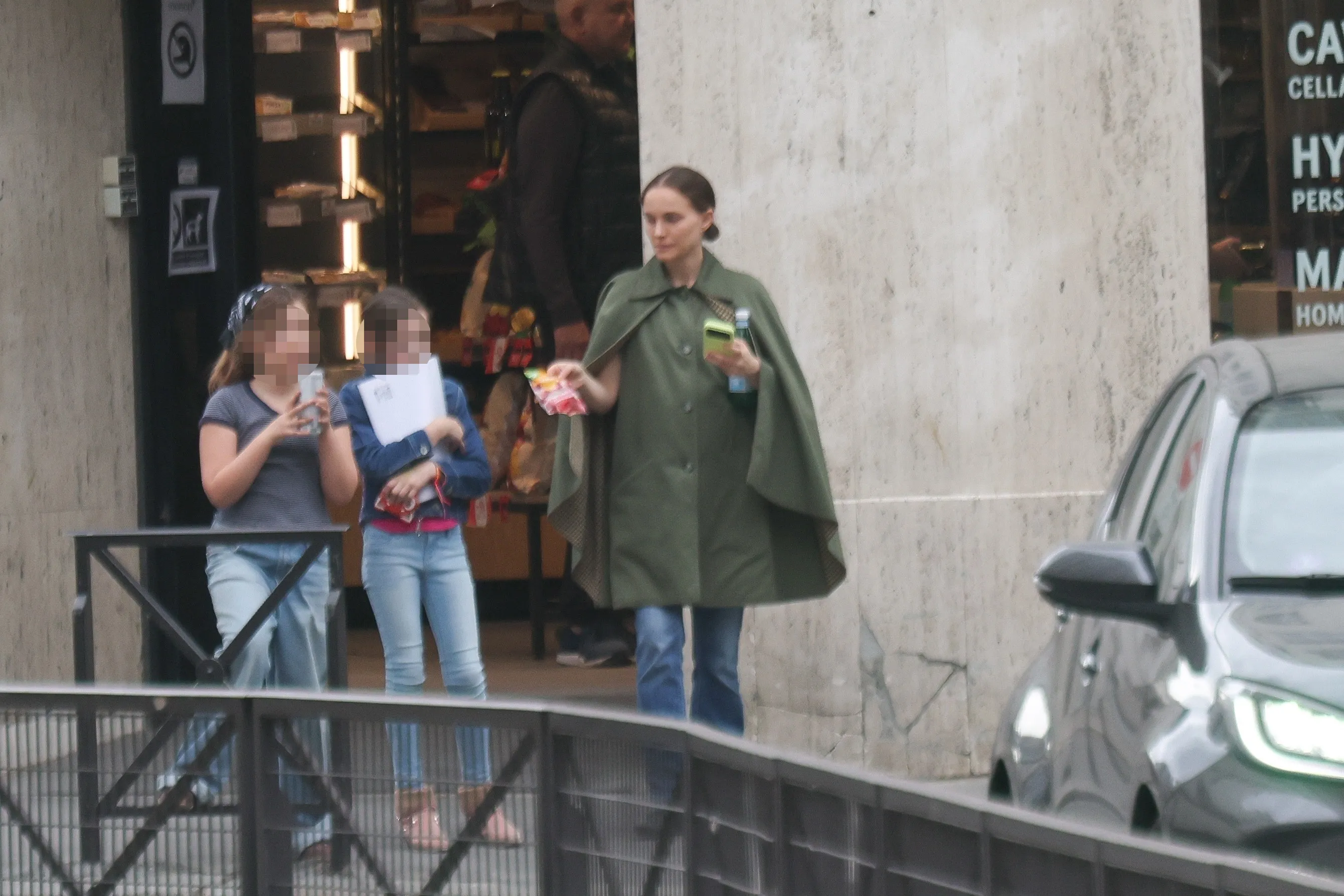 Natalie Portman walking with her daughter while holding a phone and water bottle.