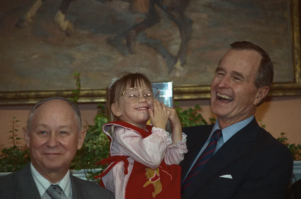 President Bush laughing as Jessica McClure tries on his glasses.