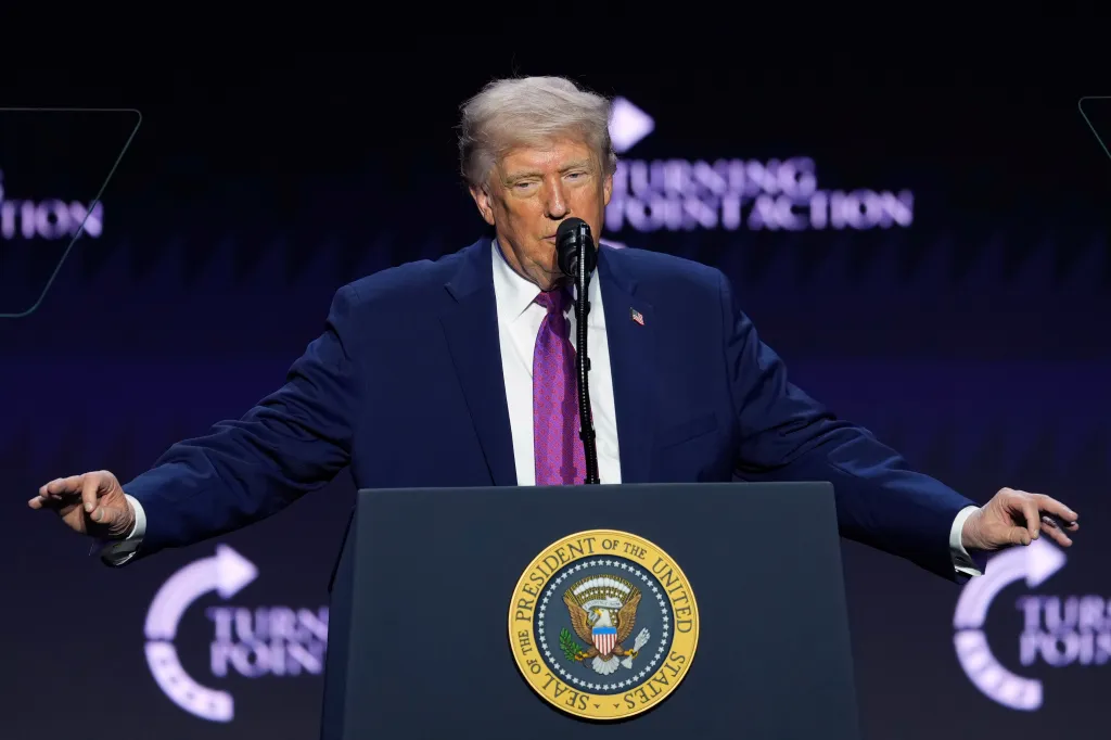Donald Trump speaking at a Turning Point USA event from a podium with the Seal of the President of the United States.