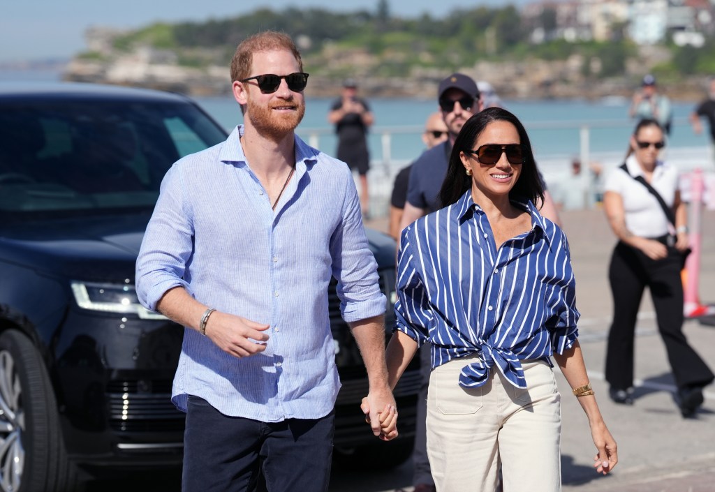 Prince Harry and Meghan, Duke and Duchess of Sussex, holding hands while walking outside.