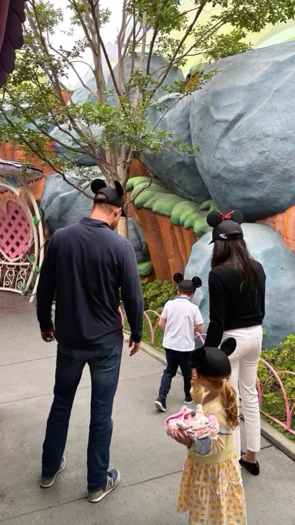 Prince Harry, Meghan Markle, Archie, and Lilibet walking away from the camera in Mickey Mouse ear hats at Disneyland.