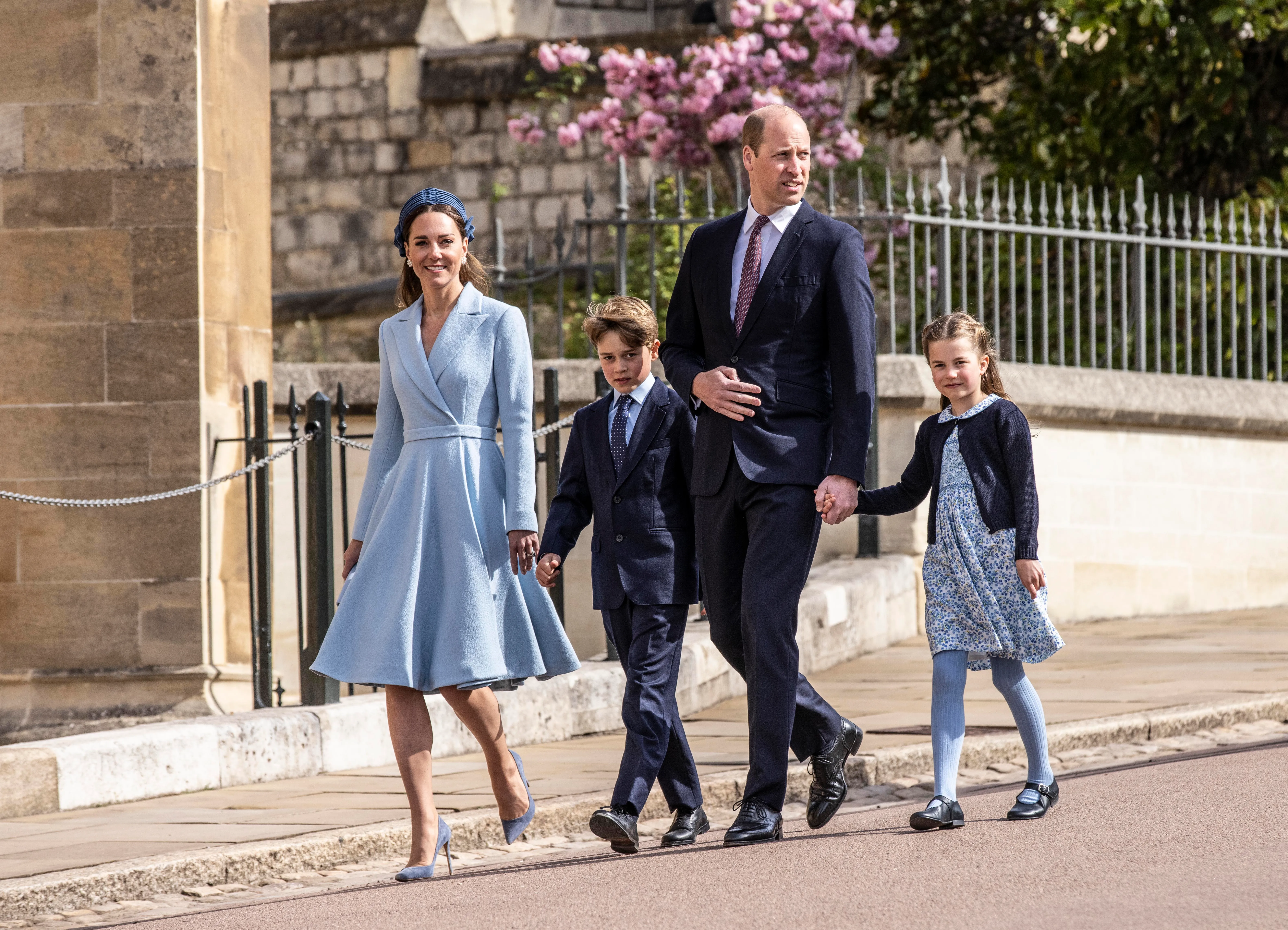 Prince William, Catherine, George, and Charlotte walking hand-in-hand outside a building.