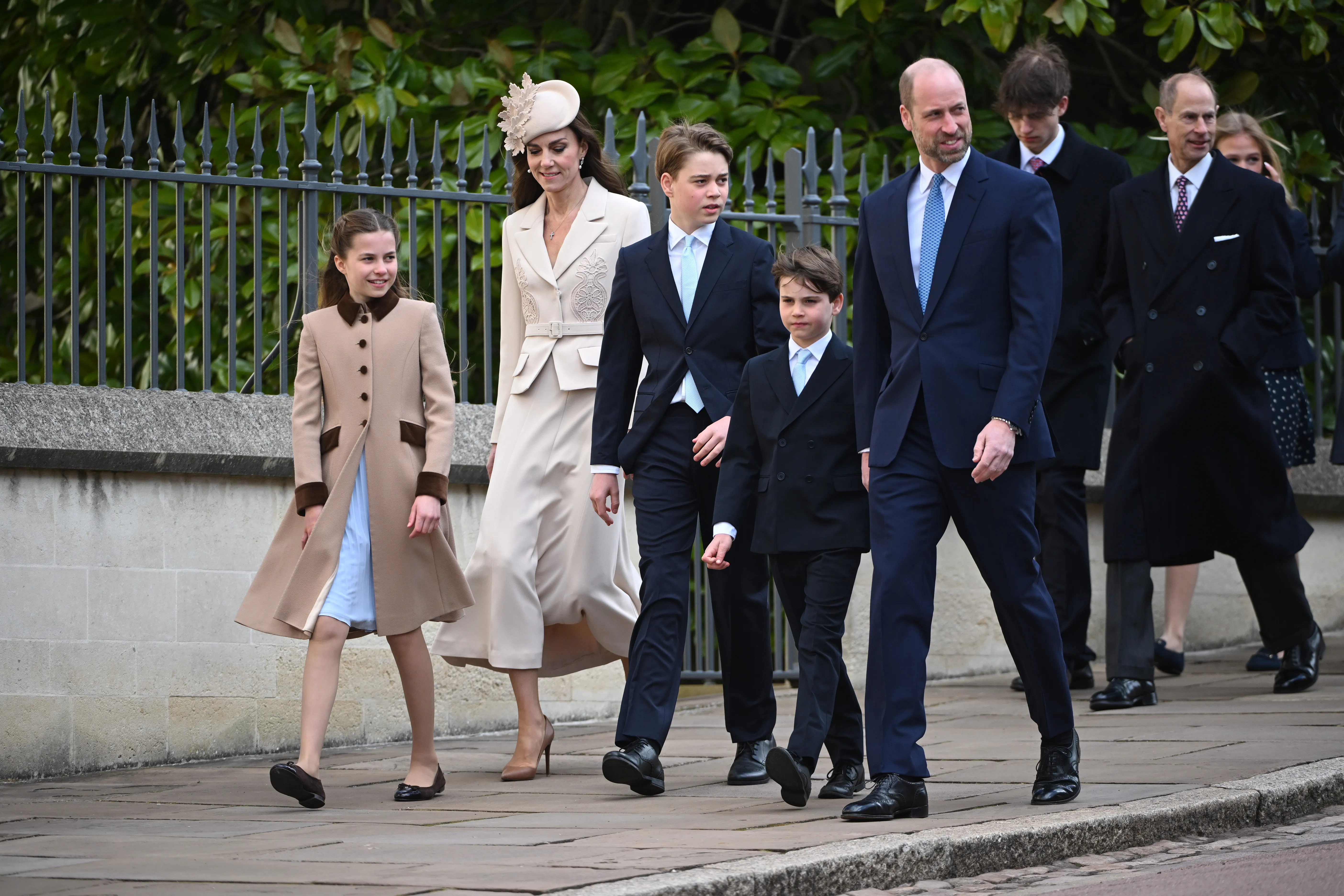 The Prince and Princess of Wales with their three children, Princess Charlotte, Prince George, and Prince Louis, walking on a paved path.