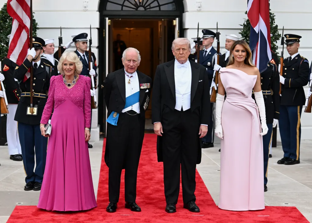 King Charles III, Queen Camilla, President Donald Trump, and First Lady Melania Trump posing on a red carpet with military personnel in the background.