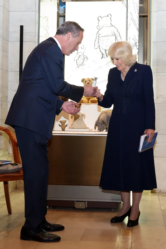 Queen Camilla, in a navy blue dress, presents a replica of Roo to Anthony Marx, CEO of the New York Public Library, in a navy blue suit.