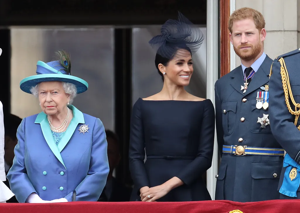 Queen Elizabeth II, Meghan Markle, and Prince Harry stand on a balcony.