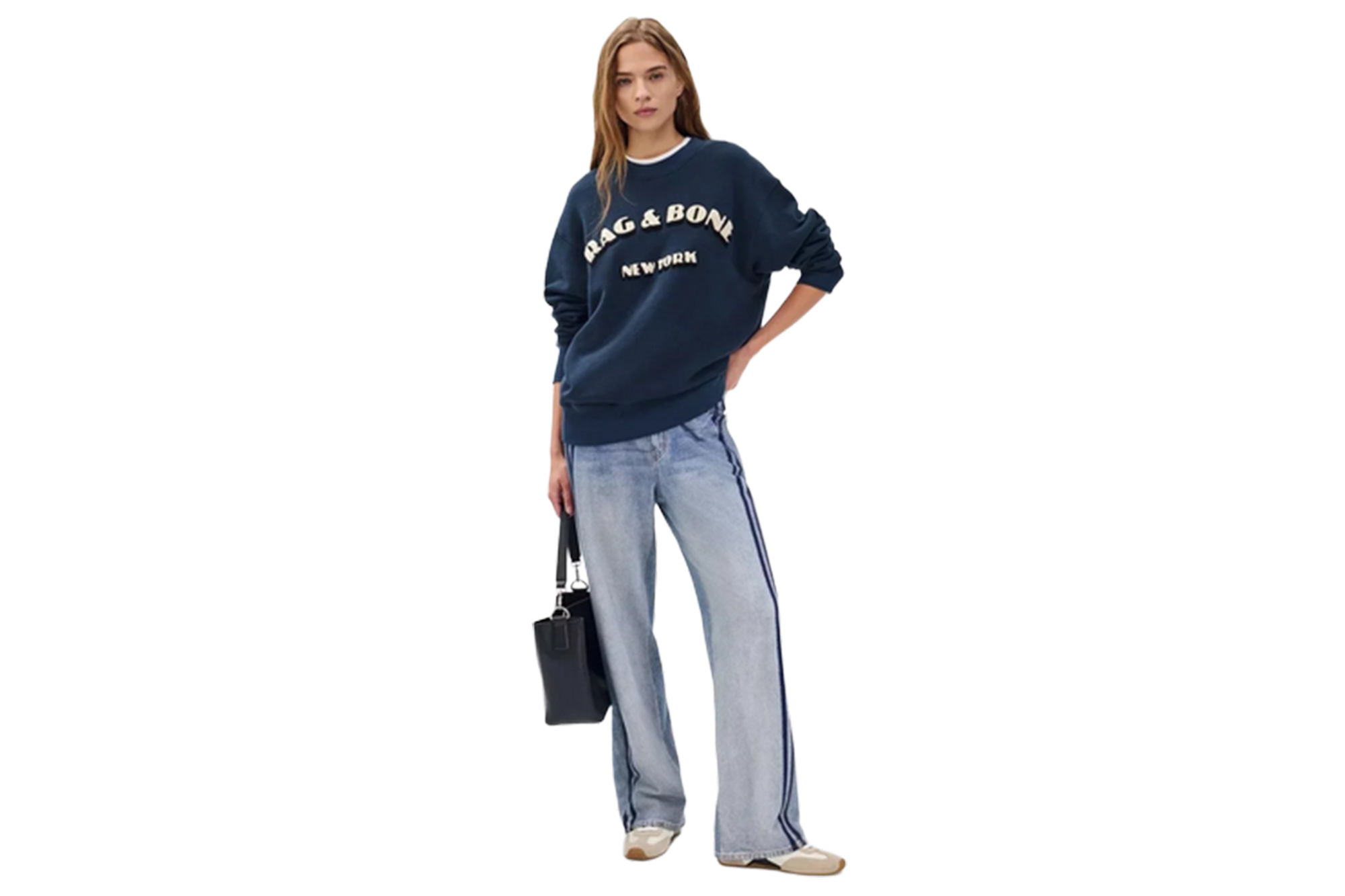 A model wearing a navy blue Rag & Bone New York sweatshirt, light wash jeans with a navy stripe, and carrying a black bag.