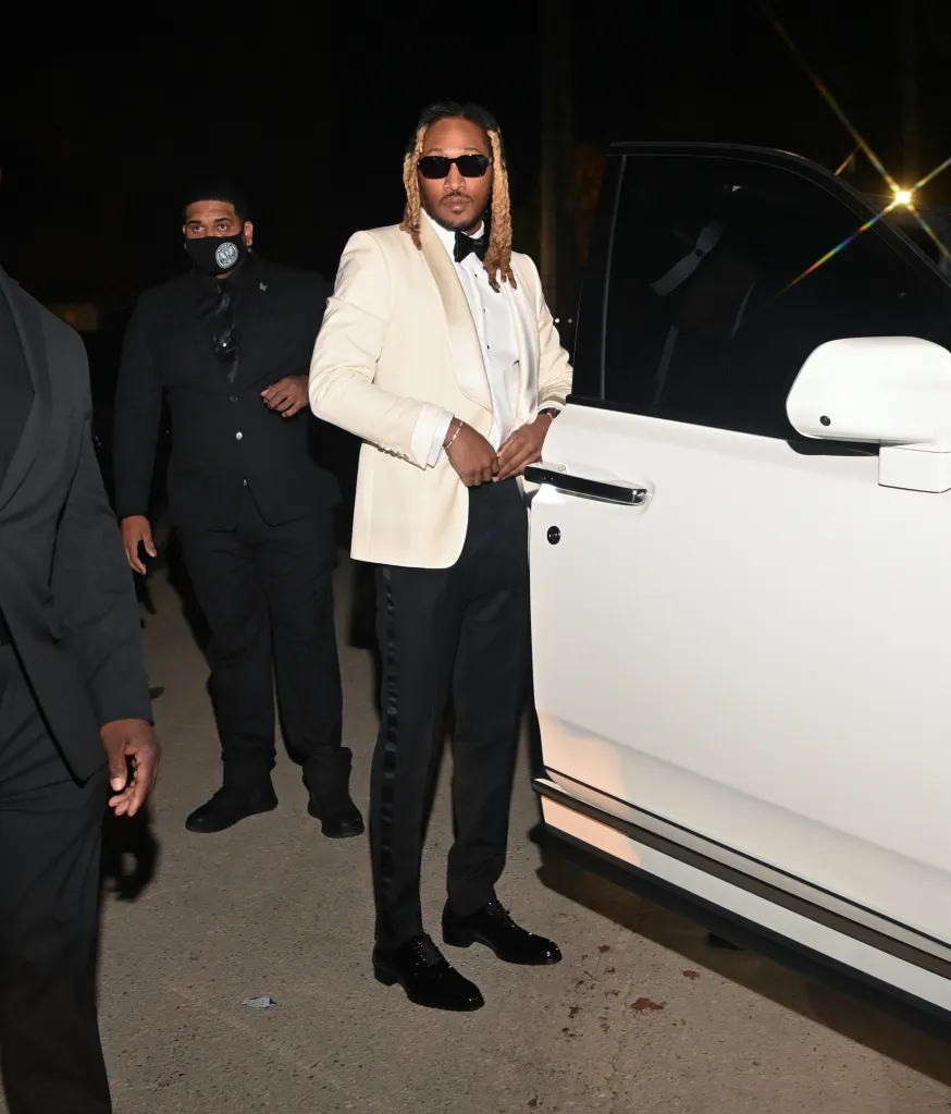 Rapper Future, dressed in a cream tuxedo jacket and black pants, standing by a white SUV.