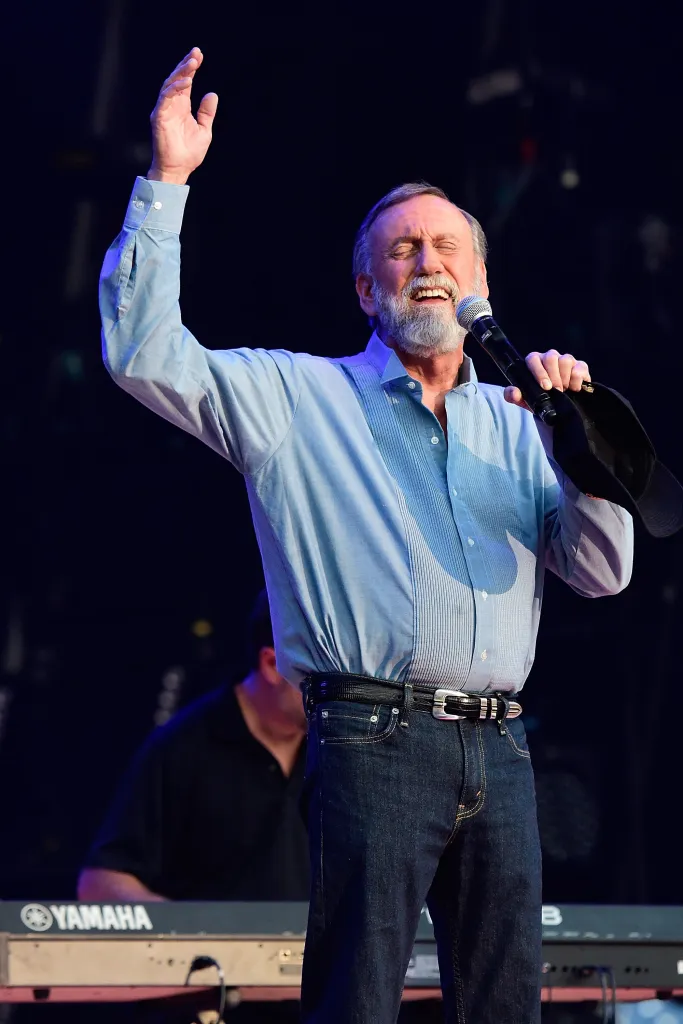 Ray Stevens singing into a microphone with his right arm raised.