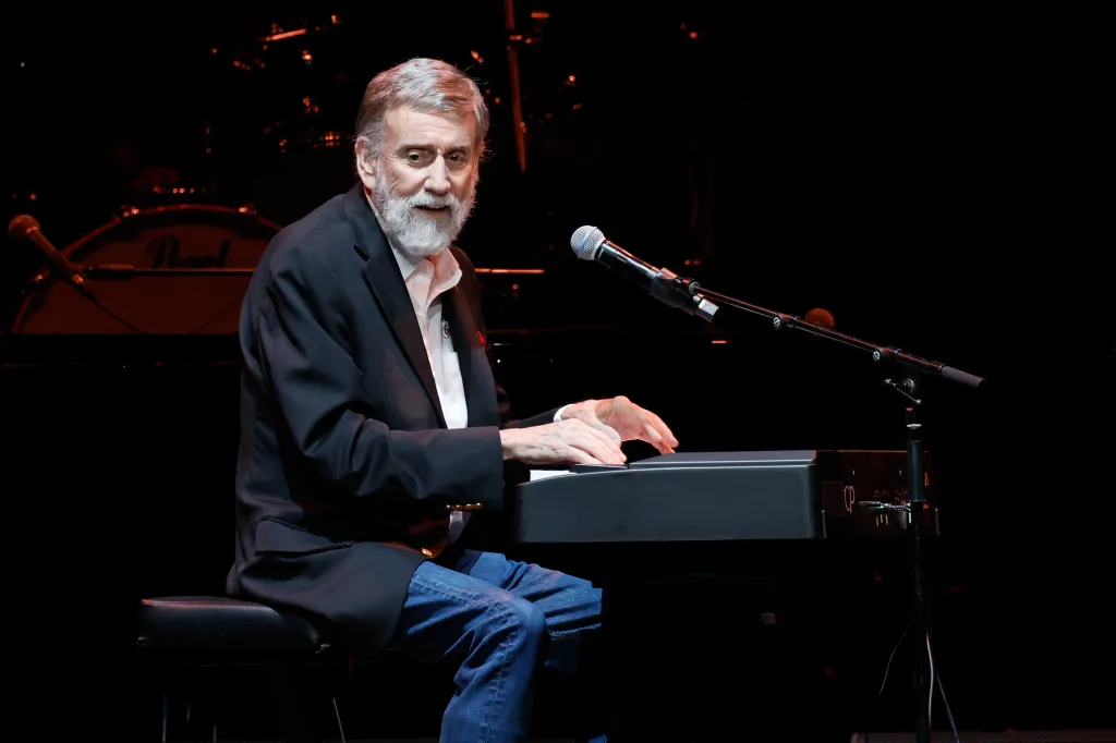 Ray Stevens performing on stage, sitting and playing a keyboard.