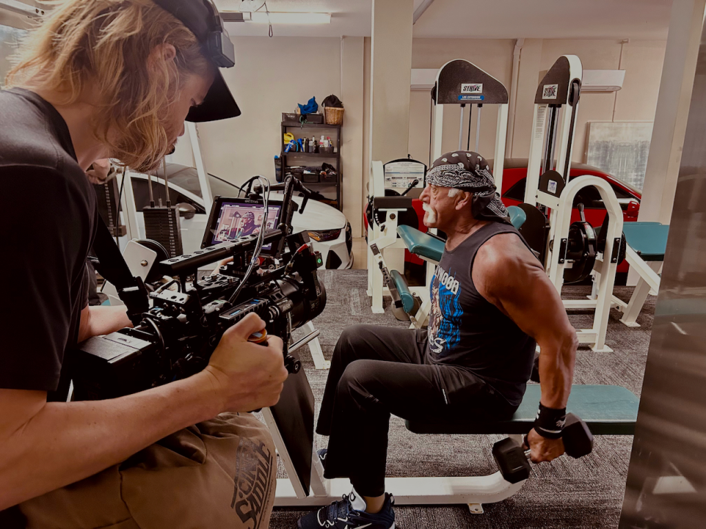 Filmmaker capturing Hulk Hogan lifting weights in a gym.