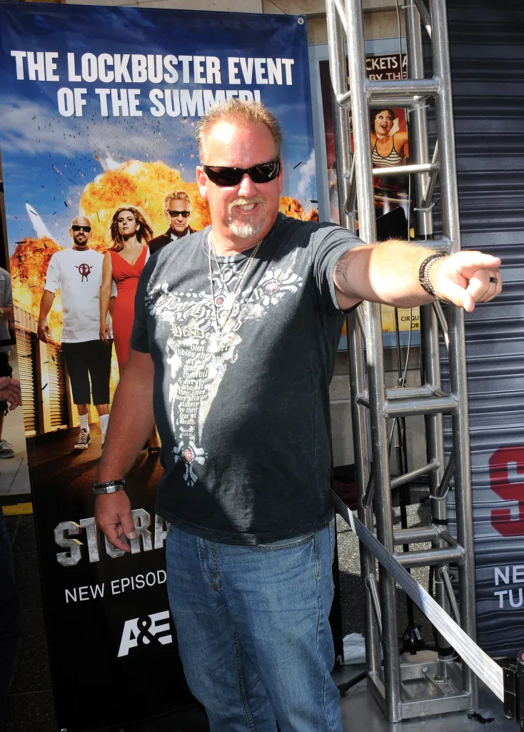Darrell Sheets wearing a black t-shirt and jeans, pointing at the camera, with a 