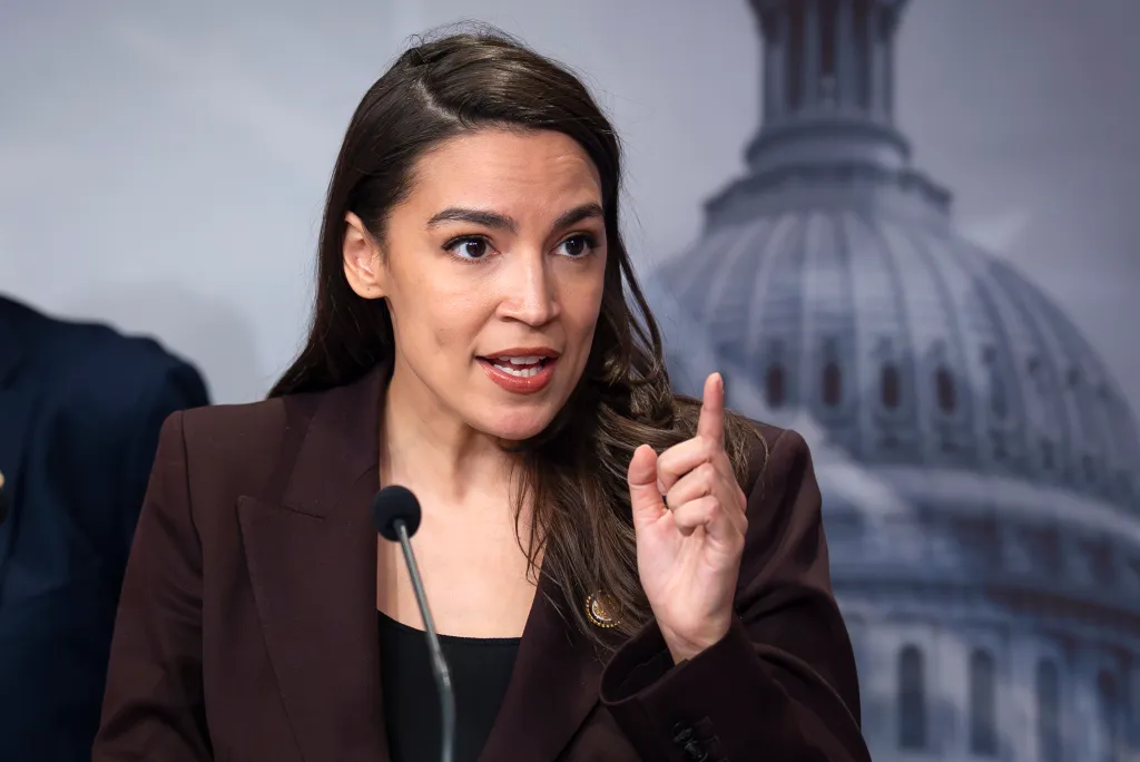 Alexandria Ocasio-Cortez speaking at a news conference in front of the Capitol dome.