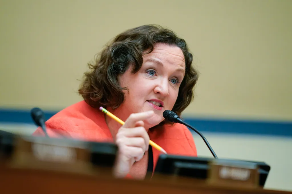 Rep. Katie Porter speaking at a hearing, holding a pencil, with a microphone in front of her.