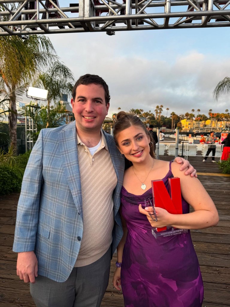 Abbey Romeo and David Isaacman smile while standing outdoors, with Abbey holding a