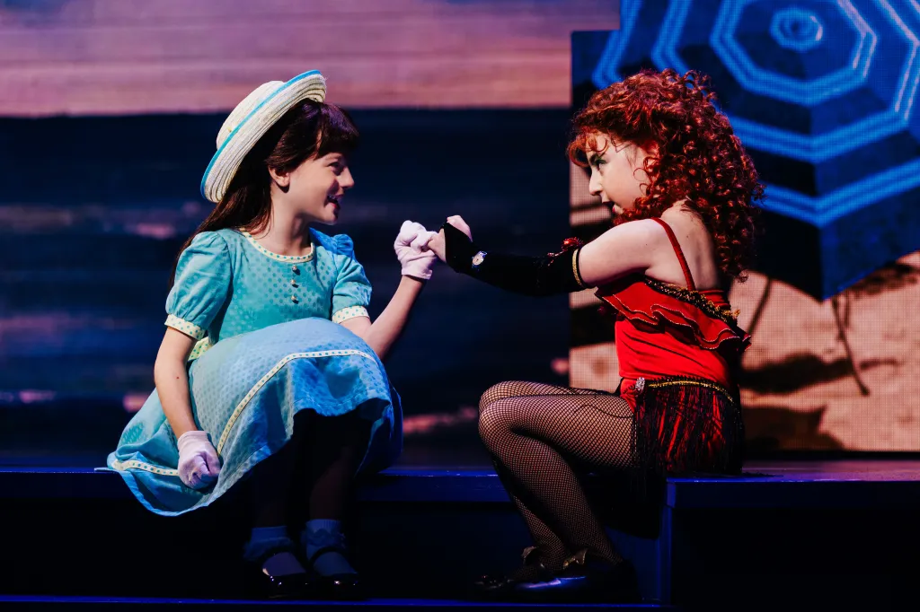 Two young actresses, Zeya Grace and Samantha Schwartz, hold hands while in costume as Little Bertie and Little Cee Cee.