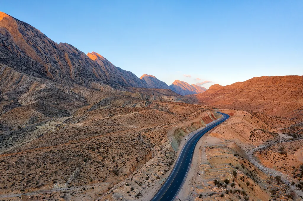 An aerial view of a winding asphalt road through the rugged Zagros Mountains in South Iran at sunset.