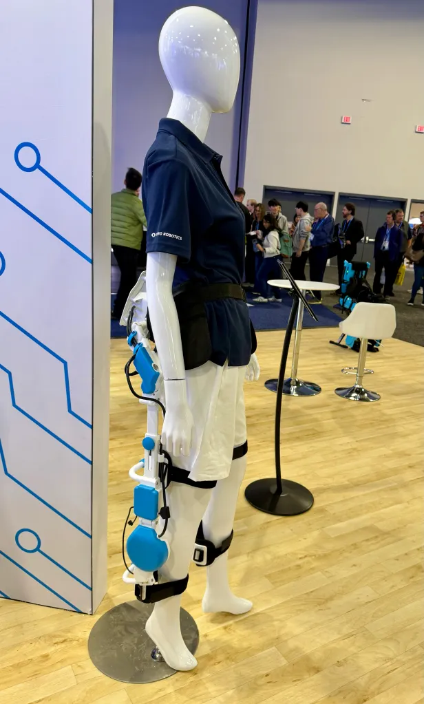 Mannequin wearing a blue and white robotic exoskeleton on its left leg.