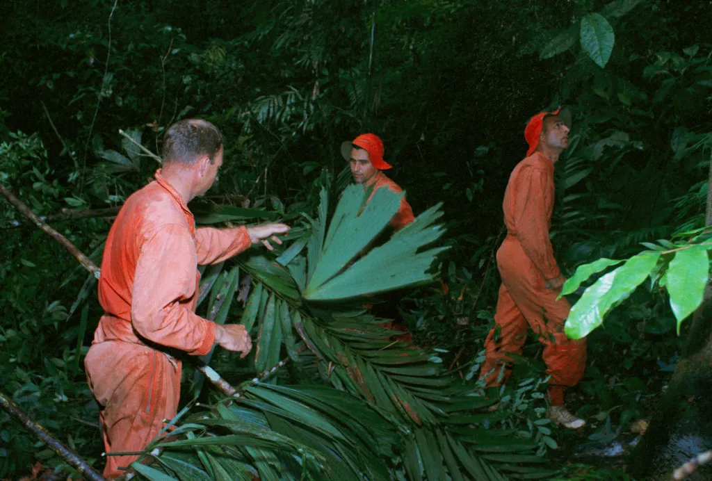 Three astronauts in orange suits during jungle survival training.