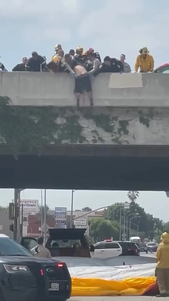 Police and firefighters rescue a man dangling over a freeway overpass.