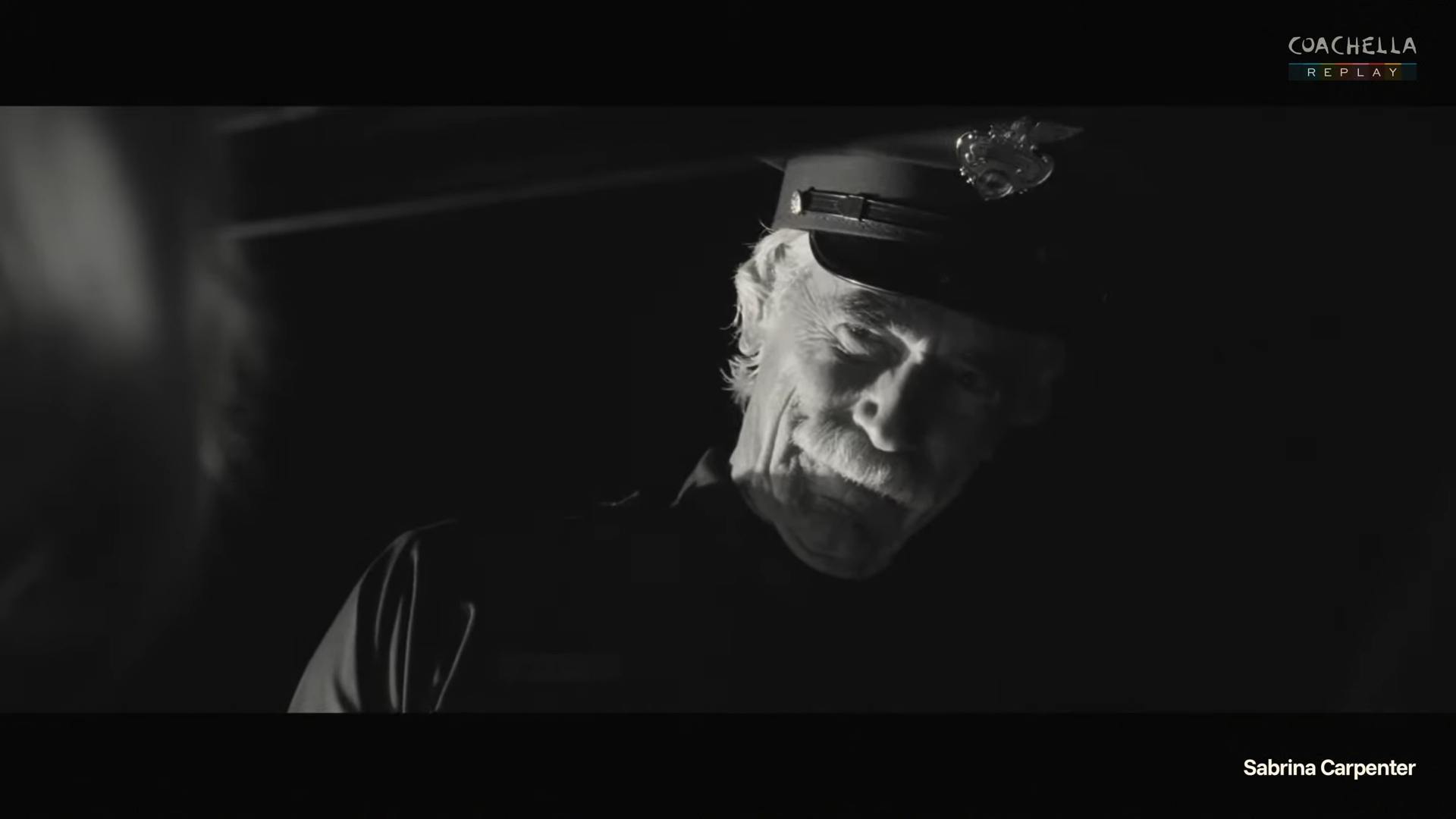 Sam Elliott dressed as a police officer on a dark stage.