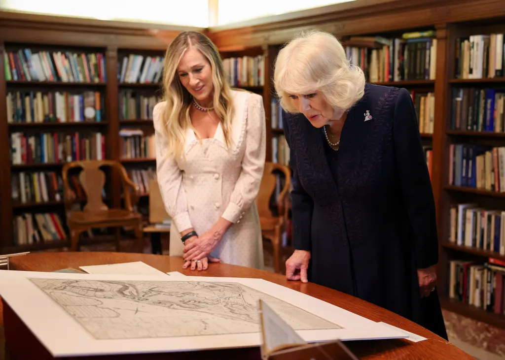 Sarah Jessica Parker, in a cream dress, and Queen Camilla, in a navy blue dress, examining artifacts at the New York Public Library.
