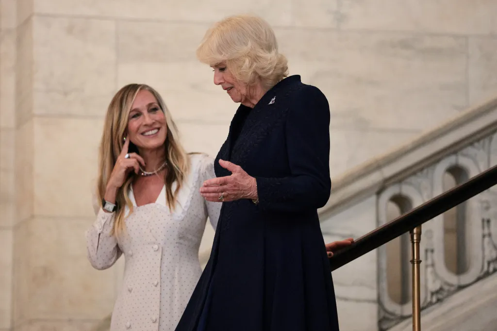 Sarah Jessica Parker, in a cream dress, speaking with Queen Camilla, in a navy blue dress, at a literacy event.