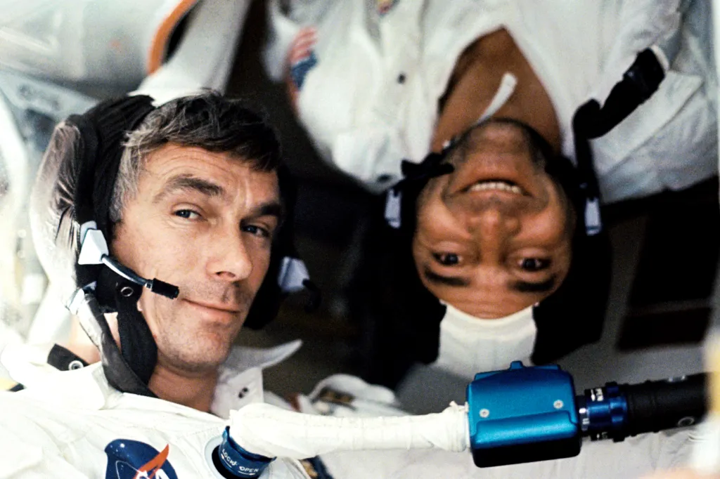 Two astronauts in white suits and headsets, one right-side-up, the other upside-down, pose for a photo aboard the Apollo 17 spacecraft.