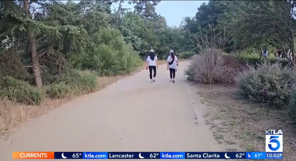 Two people walk down a dirt path surrounded by trees and bushes.