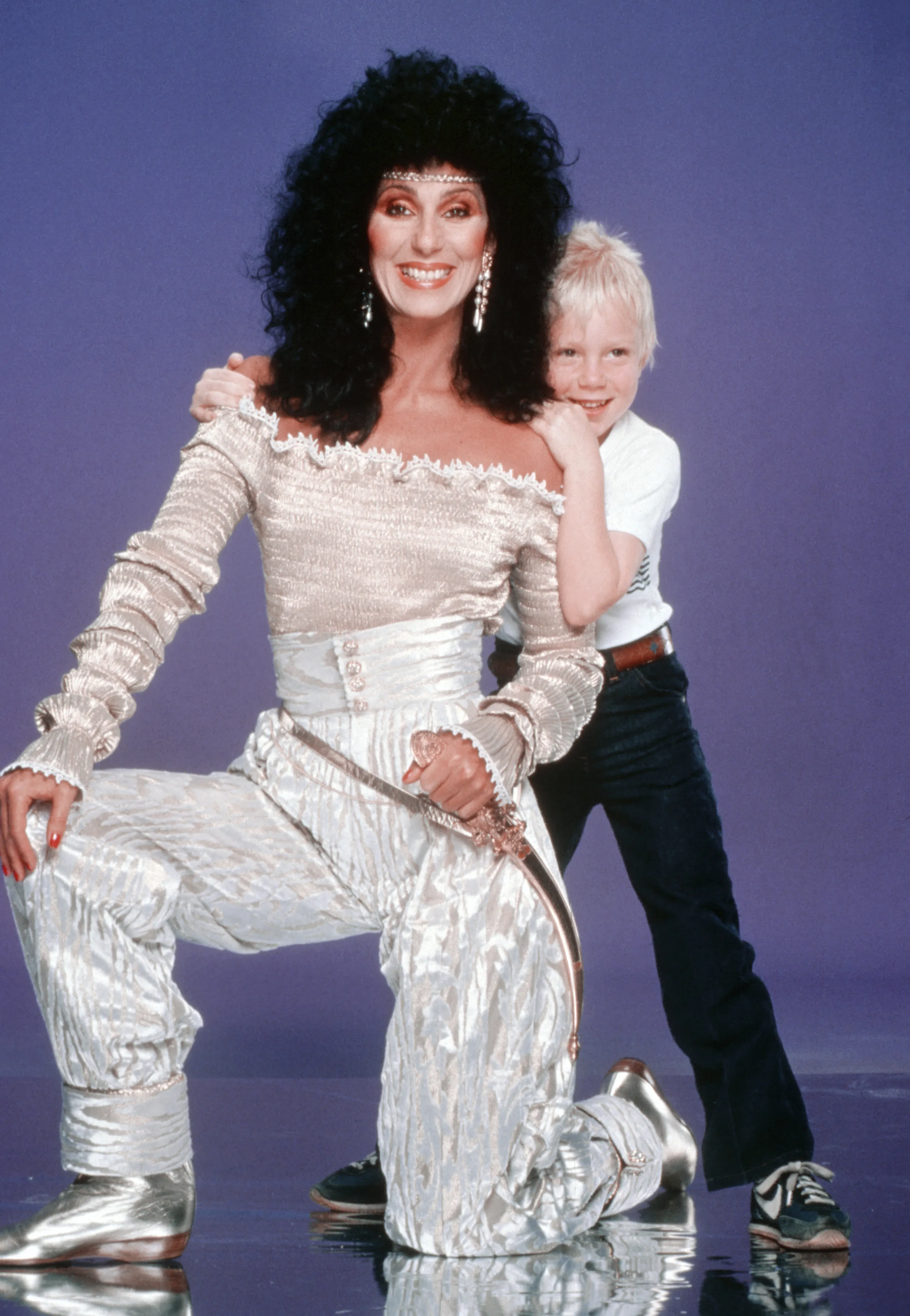 Cher kneeling with her son Elijah Blue Allman smiling behind her.