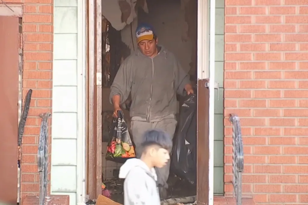 Two men carrying bags out of a fire-damaged building.