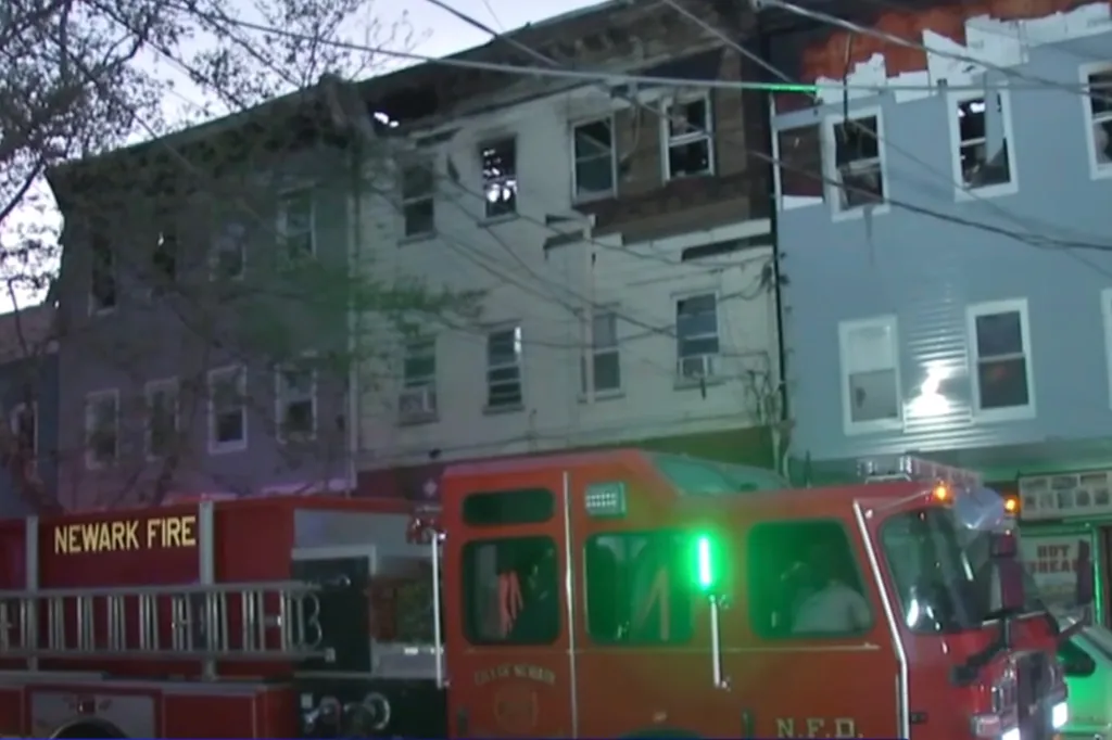 A Newark fire truck parked in front of fire-damaged buildings with broken windows.